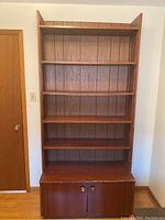 Front view of the tall six shelf book shelf with double cupboard at bottom. Wood finish with vertical paneling on back.