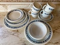 Overall view of set showing stacked plates, bowls, cups with saucers on marble countertop.