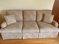 Full front view of a yellow paisley fabric three seater sofa with three reversible seat cushions and two matching throw cushions arranged at each end.