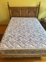 Full bed setup showing mattress and box spring on metal frame with wood headboard against yellow wall.