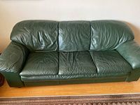 Front view of dark green leather sofa showing three cushion seating with noticeable leather wear and creasing.