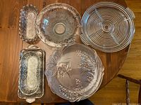 Overview of all items showing different glass bowls and platters with silver trim and etched floral designs on wood table