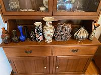 Full view of the vases displayed on a wooden cabinet shelf showing variety of sizes, shapes, and colors.