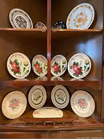 Various vintage and decorative plates arranged on wooden shelves featuring floral and bird motifs with Sovereign Potters Canada hand painted set prominently displayed.