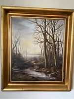 Full view of the signed oil painting showing a leafless tree landscape, small stream, and cloudy sky with a golden frame having some corner damage.