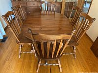 View of entire dining table with six matching chairs arranged around it showing table top surface and chair backs, wood grain and finish, as well as chair style.