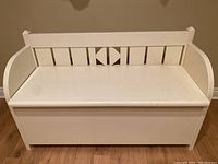Front view of the white painted wooden storage bench showing geometric cutout back and hinged top lid closed