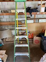 Front view of the 20-foot green and yellow metal ladder with a wooden top platform, showing the ladder standing open with visible metal steps and braces.