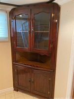 Full view of wood corner hutch showing two glass doors on top and double wooden doors on bottom, placed in basement corner.
