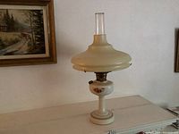 Full view profile of the antique Aladdin oil lamp showing the milk glass base with floral design and the wide pale yellow glass shade with clear chimney.