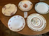 Set of five antique fine china serving plates displayed on wooden table, including Grimwades and Copeland Buttercup plate.