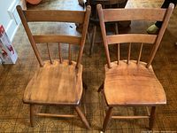 Front view of the pair of wooden chairs with chicken coop style backs and burled pine seats, showing full chair structure and natural wood color.