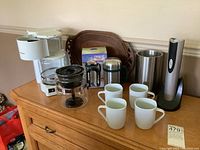 Photo of lot showing vintage Proctor Silex coffee maker with glass carafe, vintage Melitta 6-cup coffee maker missing glass topper, four white ceramic mugs, stainless steel thermal cup in box, and an Oster electric wine opener and chiller.
