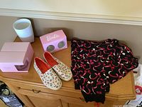 Front view of all items together on wooden cabinet: pink boxes with wine glasses, white textured vase, Toms sneakers with dog faces, flamingo print pajamas folded.