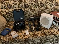 Wide view of all items included in the lot laid out on a floral patterned couch, showing the grooming kit, hair dryer, curling iron, heater, power strip, and blue leash.