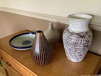 Side view of all four pieces: white/brown Gesso chalkware vase, mango wood vase, green/beige ceramic vase, and decorative bowl