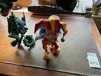 Photo showing a green dragon marionette puppet and a jester marionette puppet on a wooden surface, highlighting details of their forms and colors.