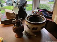 Large brown and beige ceramic planter and brown ceramic lamp together on a table near window