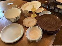 Overview of all pottery items on the table including large bowl, mugs, plates, candle holder, and platter