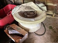 Top view of large round fire pit with faux cement finish, covered partially with a fabric cover and showing faux logs inside.