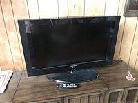 Front view of the Samsung TV with remote placed on the wooden surface in front of the TV.