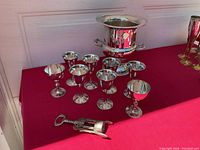 Full view of the silverplate champagne ice bucket, stemmed goblets and smaller goblets arranged on a red surface