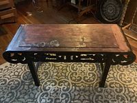 Angle photo of rectangular solid wood table with carved edge trim, showing surface wear and wood discoloration.