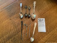 Photo of the full set of 9 various sterling silver spoons and kitchen utensils arranged on wood surface.