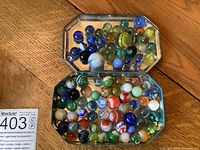 Top view of two octagonal tins filled with assorted colourful glass marbles of various sizes on a wooden floor