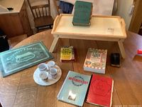 Overview of wooden breakfast tray with cookbooks stacked on top, four white espresso cups with saucers on a plate to the left, black glass hot plate to the right, and round marble hot plate on table.