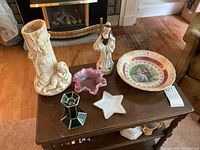 View of all vintage decorative items on a wooden table including star-shaped milk glass dish, figural vase, antique plate, pink Fenton-like dish, green stained glass candle holder, and figurine.