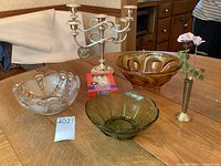 Photo showing all items on wooden table including the silver-plated five-arm candelabra with new candles, three vintage glass bowls in amber, green, and clear glass, and the small silver-plated vase with metal painted flowers.