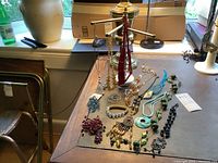 View of the three-armed dark red jewelry stand on marble base surrounded by various necklaces and jewelry items spread out on a table.