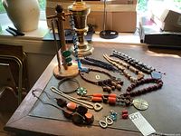 Overview of assorted necklaces and beads laid out on table with wooden display stands in background
