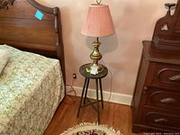 Full view of the wooden stool with the brass lamp on top beside a bed and dresser in a room setting.