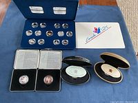 Blue case containing 12 sterling quarters and 1 Loon $1 coin from 1992 Canada 125 set along with other display boxes for additional coins.