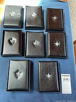 Eight closed black folio cases with maple leaf emblem arranged on blue cloth.