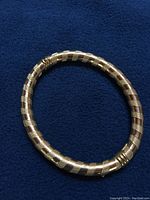 Full top-down view of oval gold bangle on dark blue fabric background