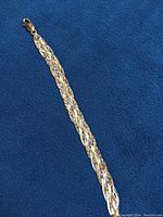 Full length of braided bracelet laid flat on blue background.