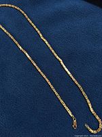 Full length of chain laid flat on dark blue fabric with lobster clasp visible at one end.