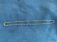 Full length view of the 10K yellow gold Singapore chain necklace laid flat on blue fabric background