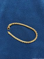 Full view of 18k yellow gold wheat bracelet on blue fabric
