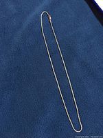 Full view of wheat chain necklace laid out on blue fabric