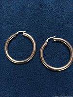 Pair of hoop earrings on dark blue textured surface, showing full shape
