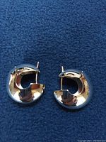 Both round huggie earrings laid flat on a blue fabric background