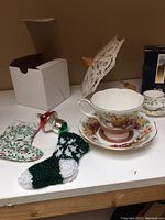 Display of teacups and saucers with Christmas ornaments including knit stockings and mushroom-shaped ornament and lace umbrella