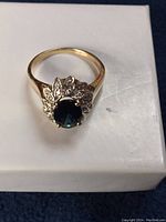 Ring face with central sapphire and diamond halo on white surface