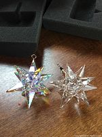 Both Swarovski crystal star ornaments on wooden surface showing size and shape