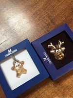 Two Swarovski ornaments in branded boxes; one gingerbread man and one reindeer head.