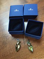 Two green Swarovski crystal Christmas ornaments displayed with their blue original boxes on a wooden table.